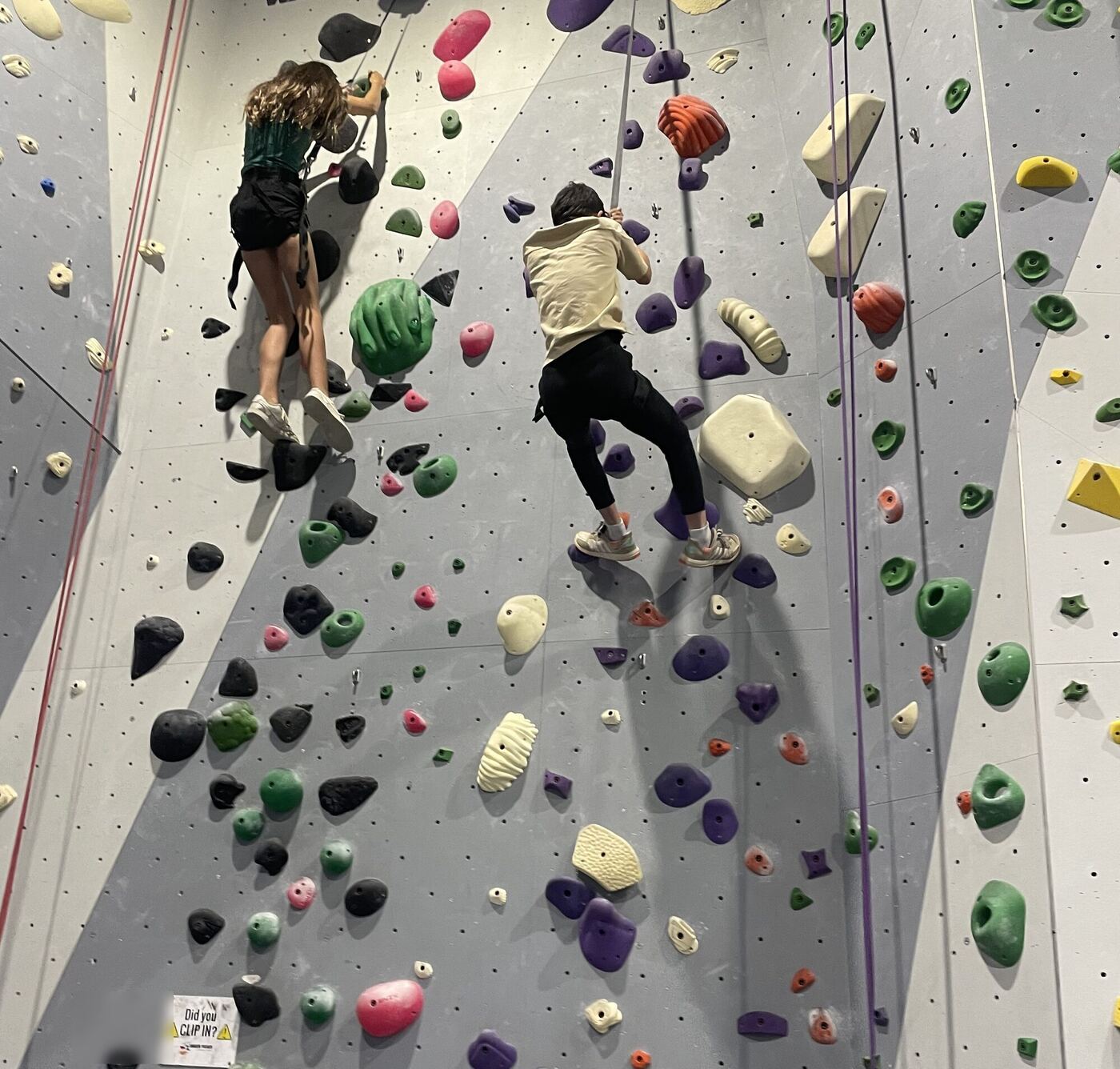 Two climbers high on a climbing wall, seen from below