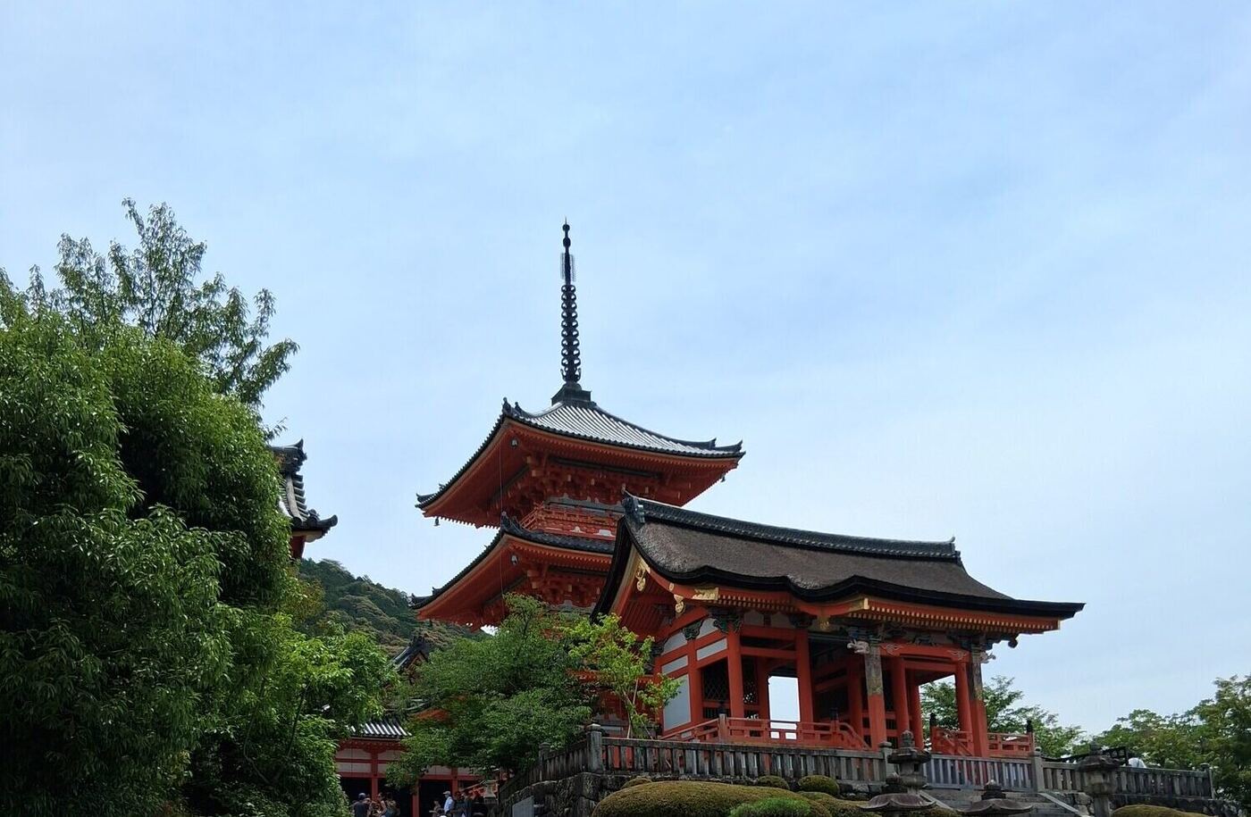 A red temple gate and pagoda above the trees in Japan