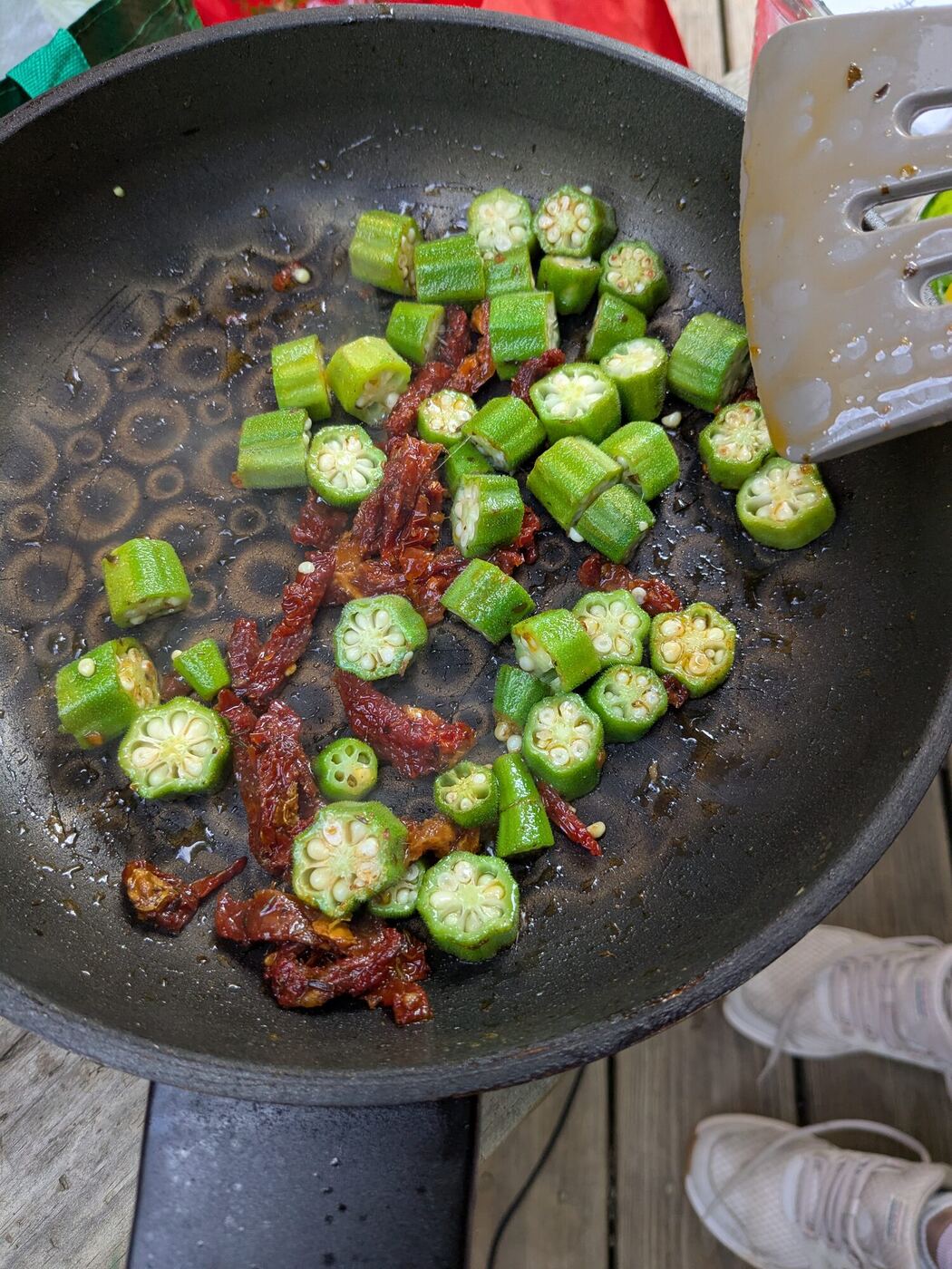 Sliced okra frying in a skillet with dried tomatoes