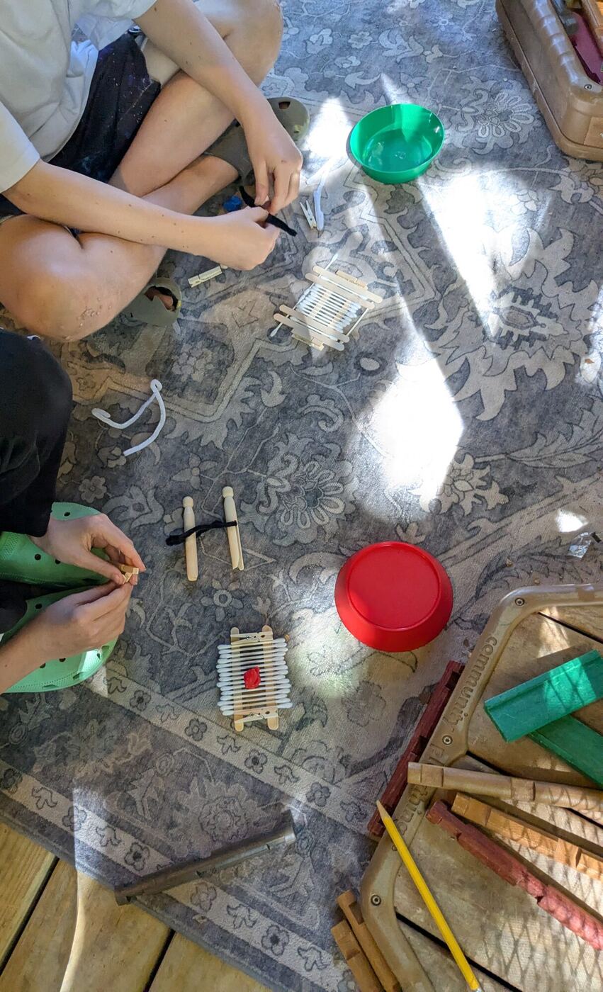 Small bridges of cotton swabs and craft sticks on a rug, hands at work on another