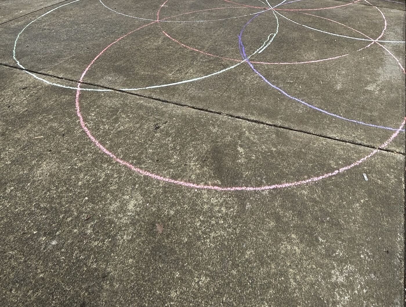 Large overlapping chalk circles in pink, white and purple on the concrete driveway