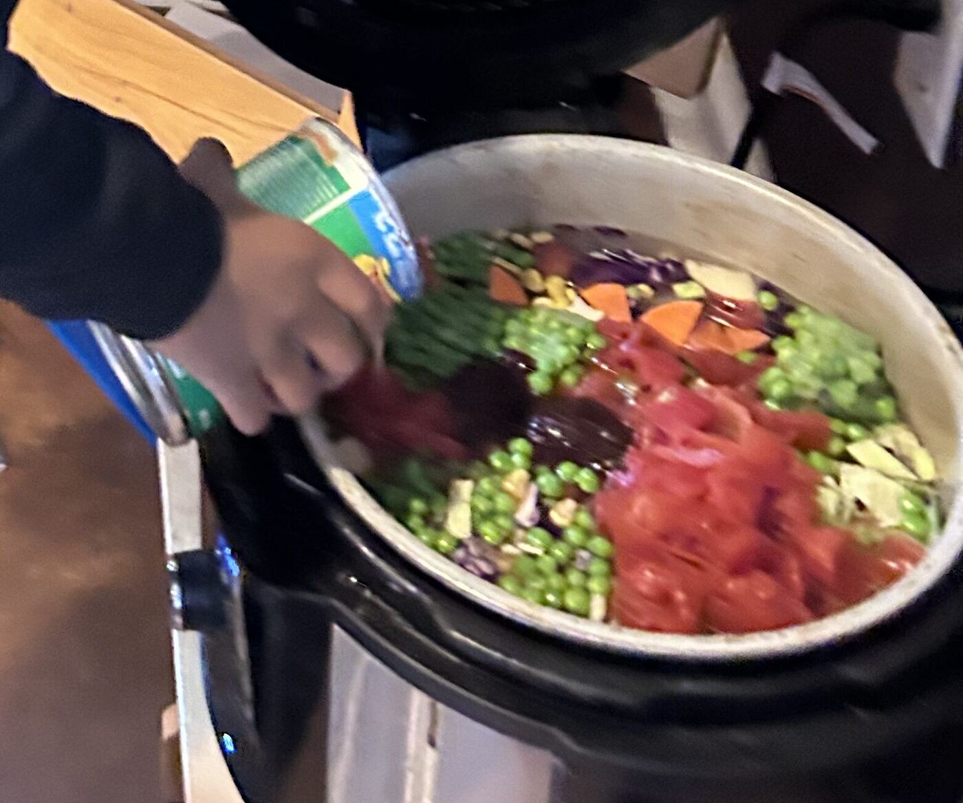 A hand pouring peas into the pot of vegetables for the soup
