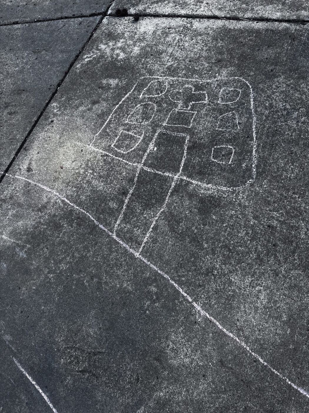 A chalk drawing of a hospital with a cross on its roof, and a chalk road, on the driveway