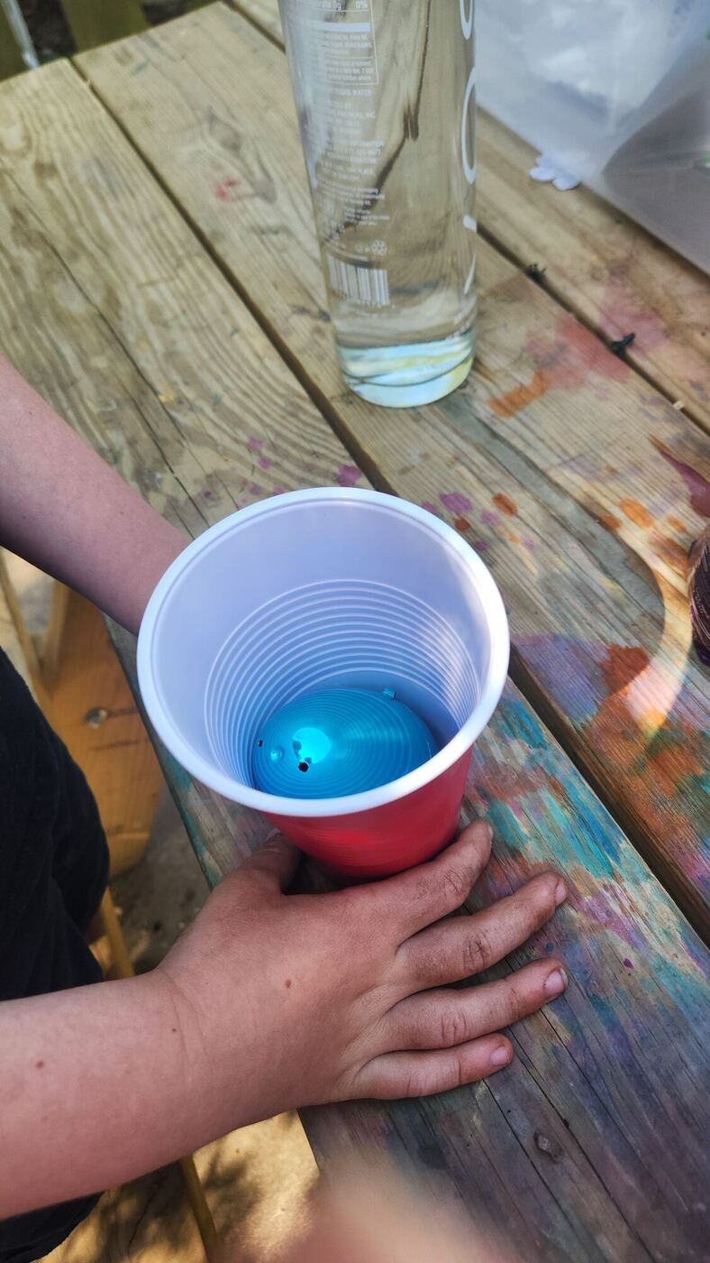A hand steadying a red and white cup with a blue plastic egg inside