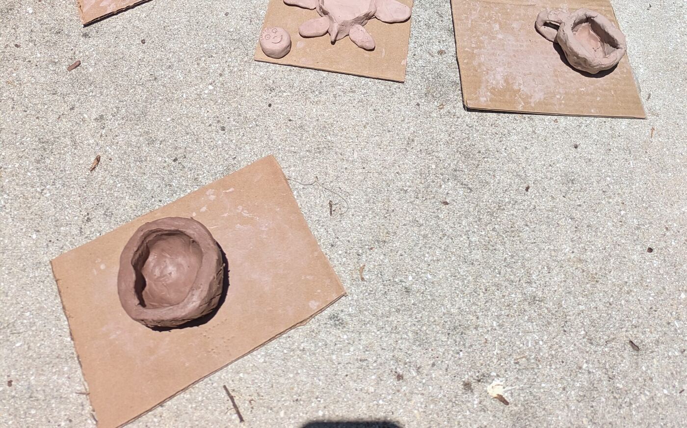 Pinch pots and a clay mug drying on squares of cardboard