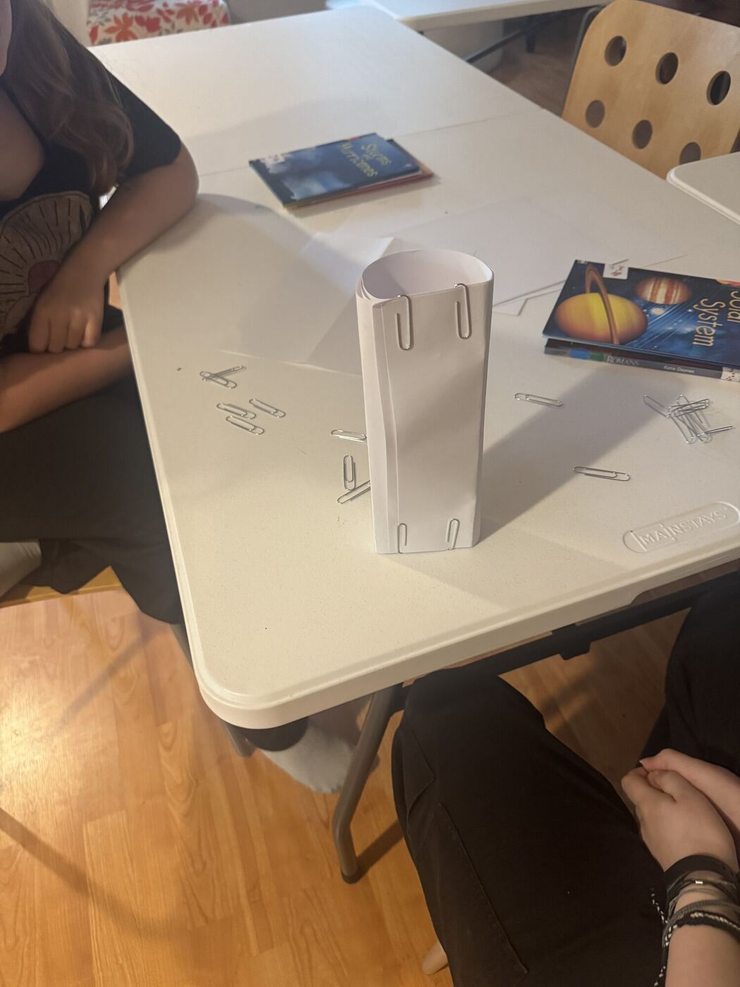 A paper tower held together with paper clips, standing on a table