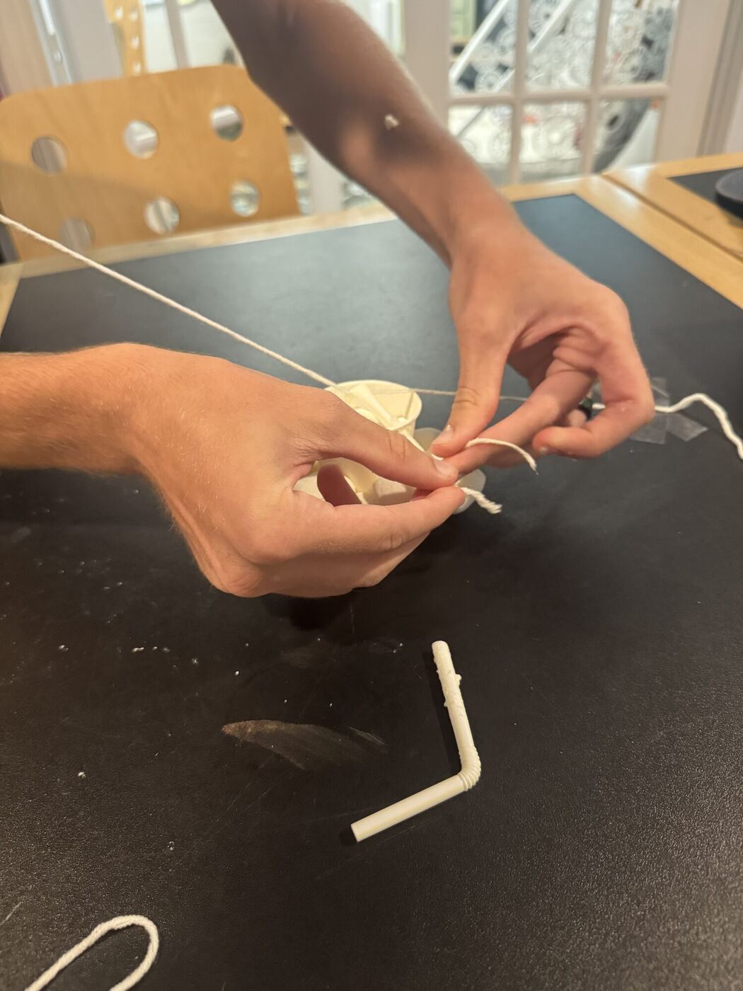 Hands threading string through a paper cup
