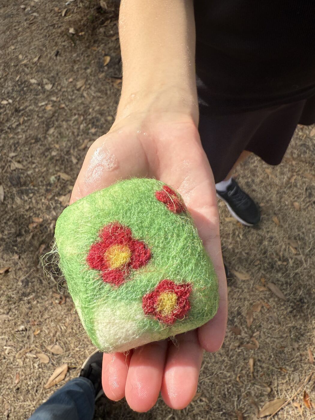An open hand holding a green felted ball with red flowers