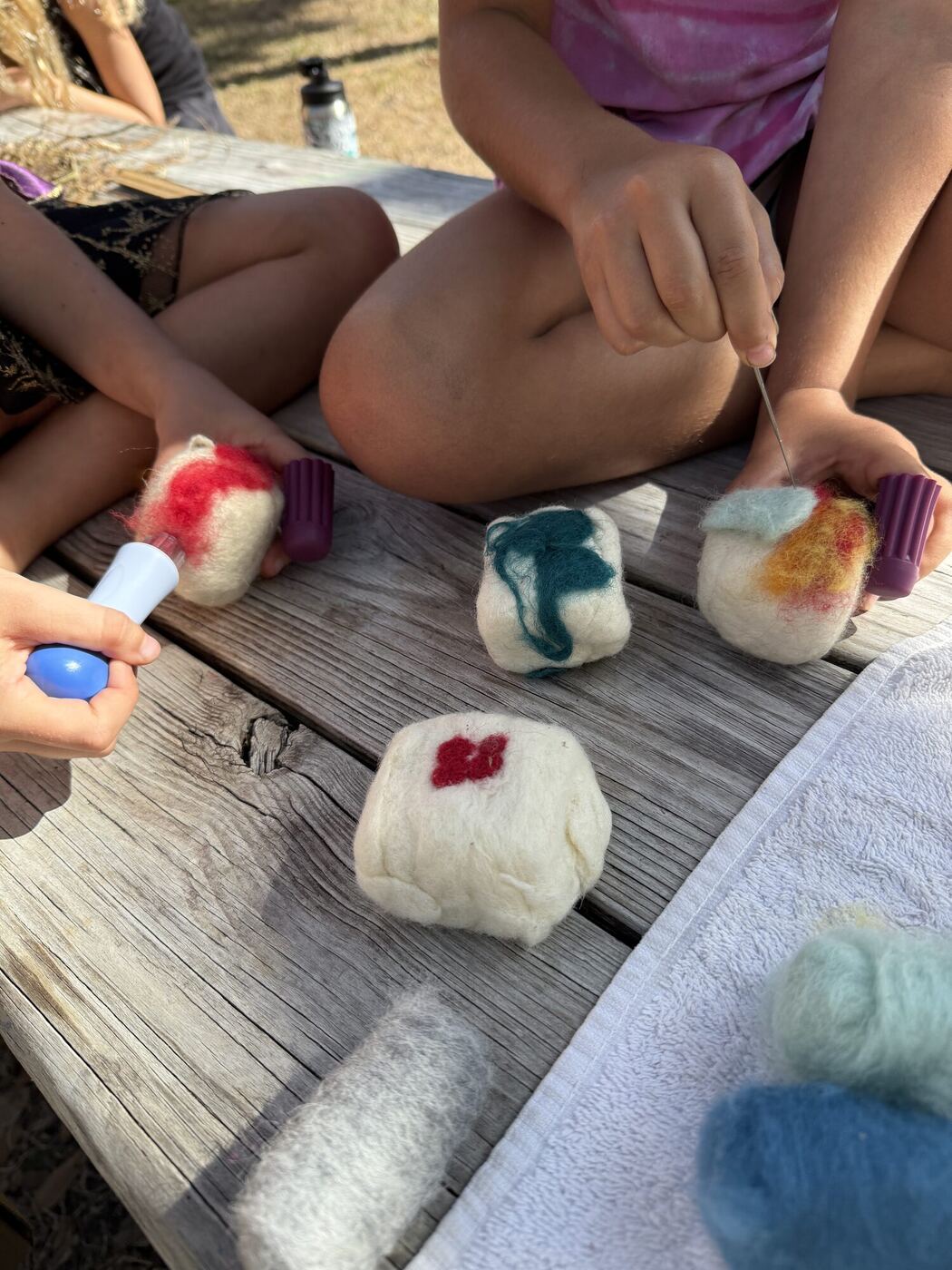 Bars of soap wrapped in wool on a picnic table, hands working a felting needle
