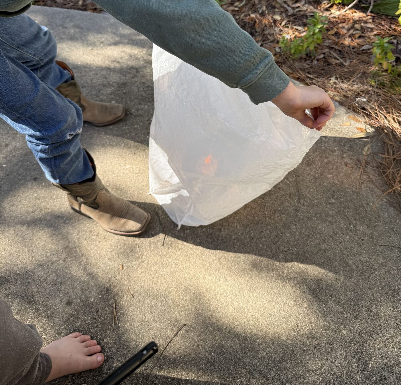 A plastic bag held open over a candle on the pavement