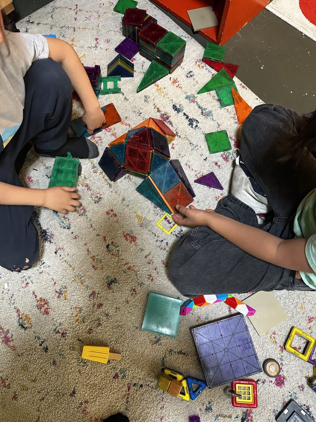 A magnet-tile building on the rug, two builders seen from above