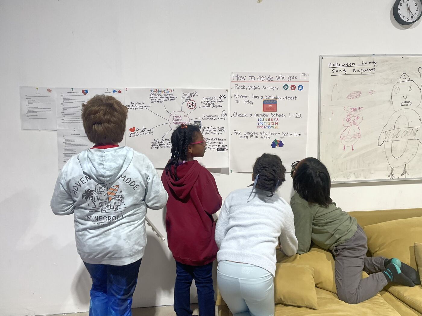 Four learners seen from behind, reading the good-sport agreements pinned to the wall