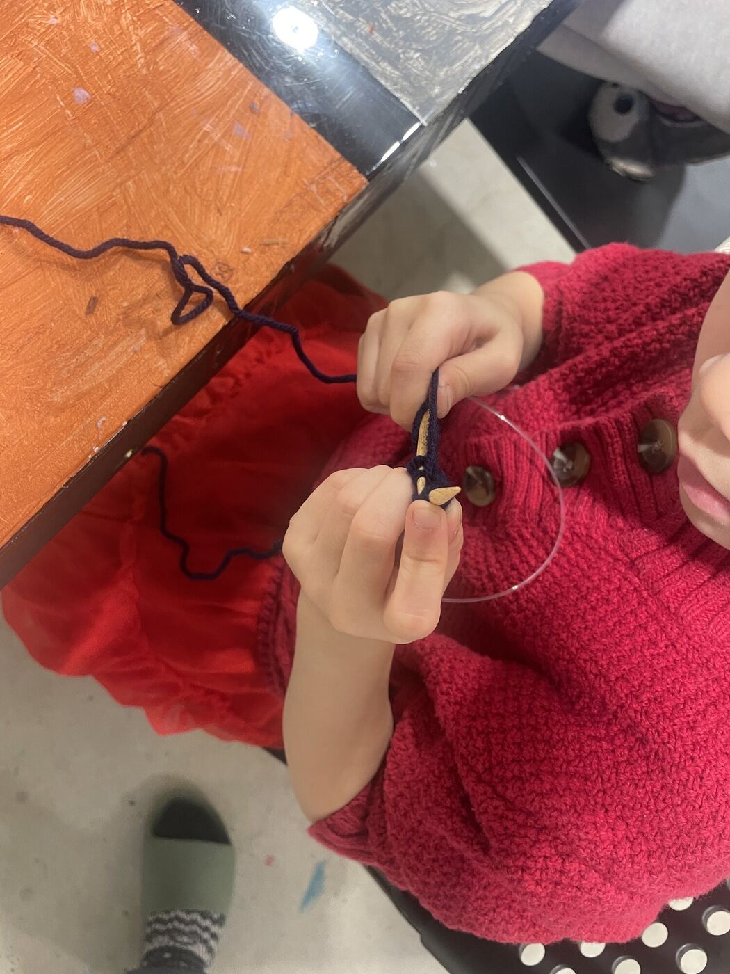 Hands working a row of knitting in red wool