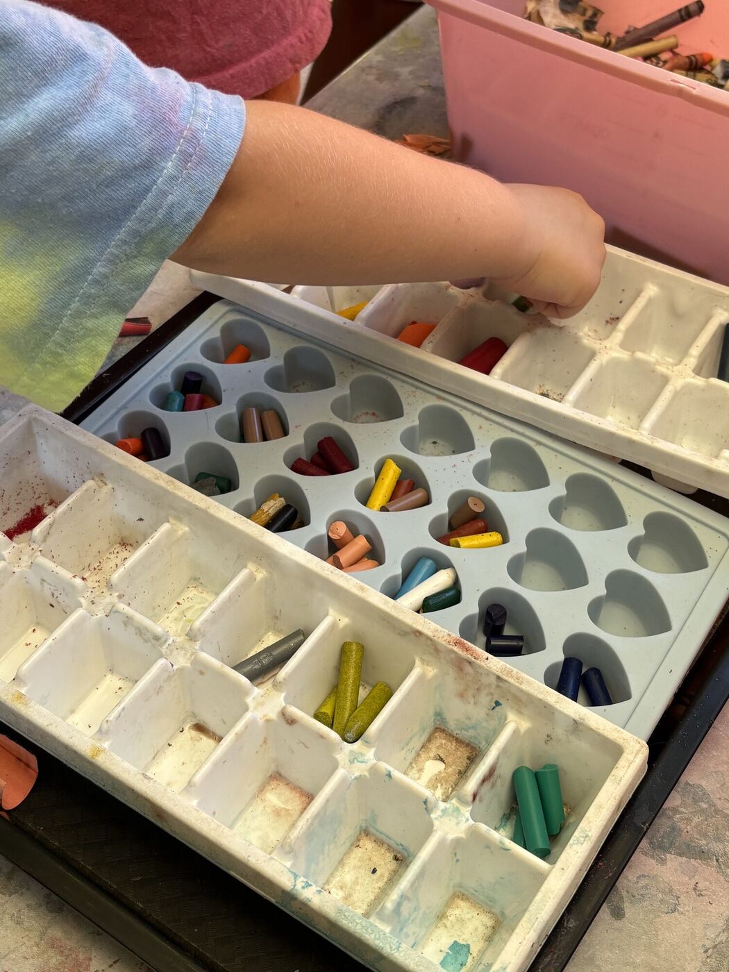 A hand dropping broken crayons into the wells of an ice cube tray