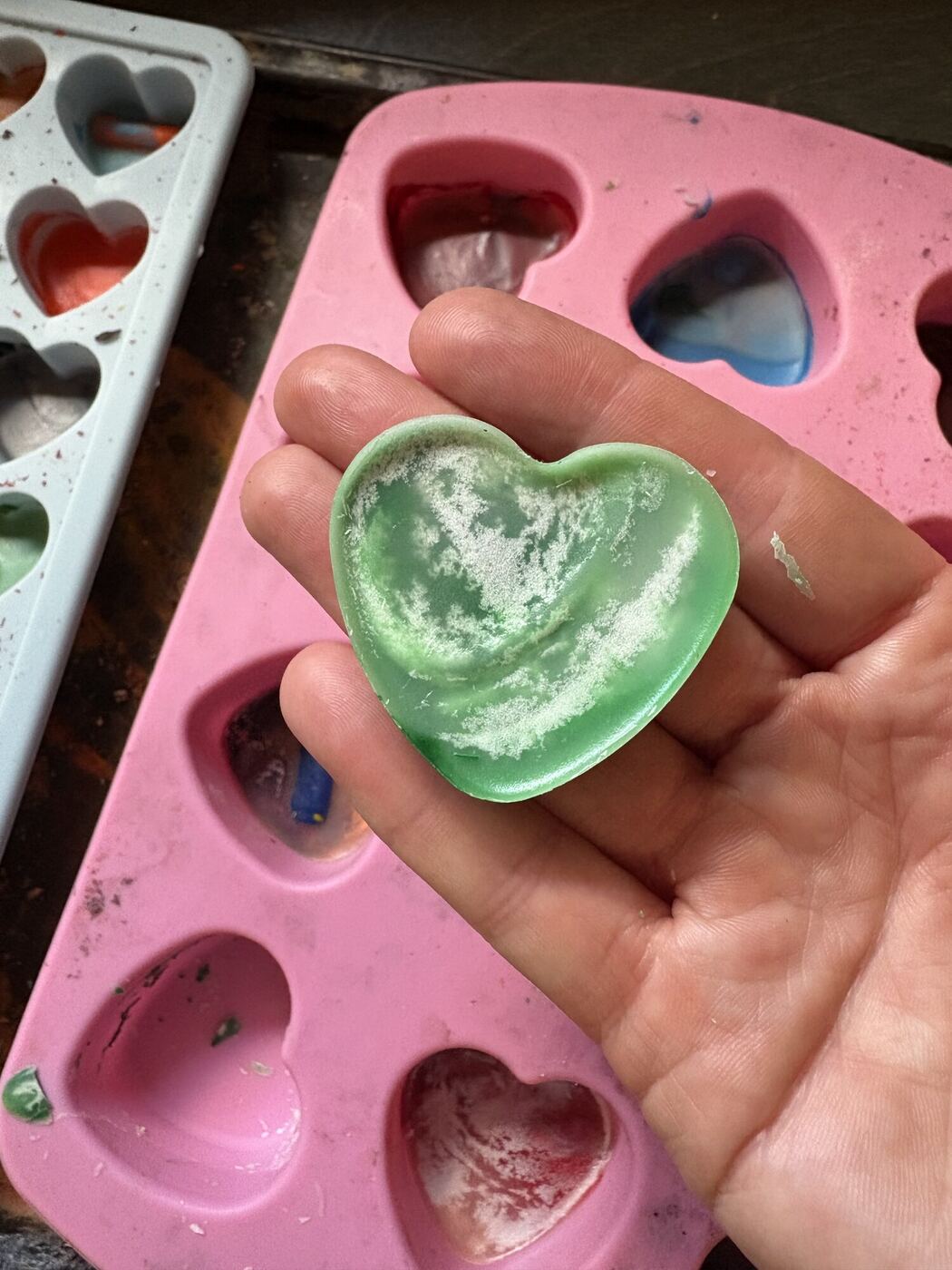A hand holding a finished green crayon heart