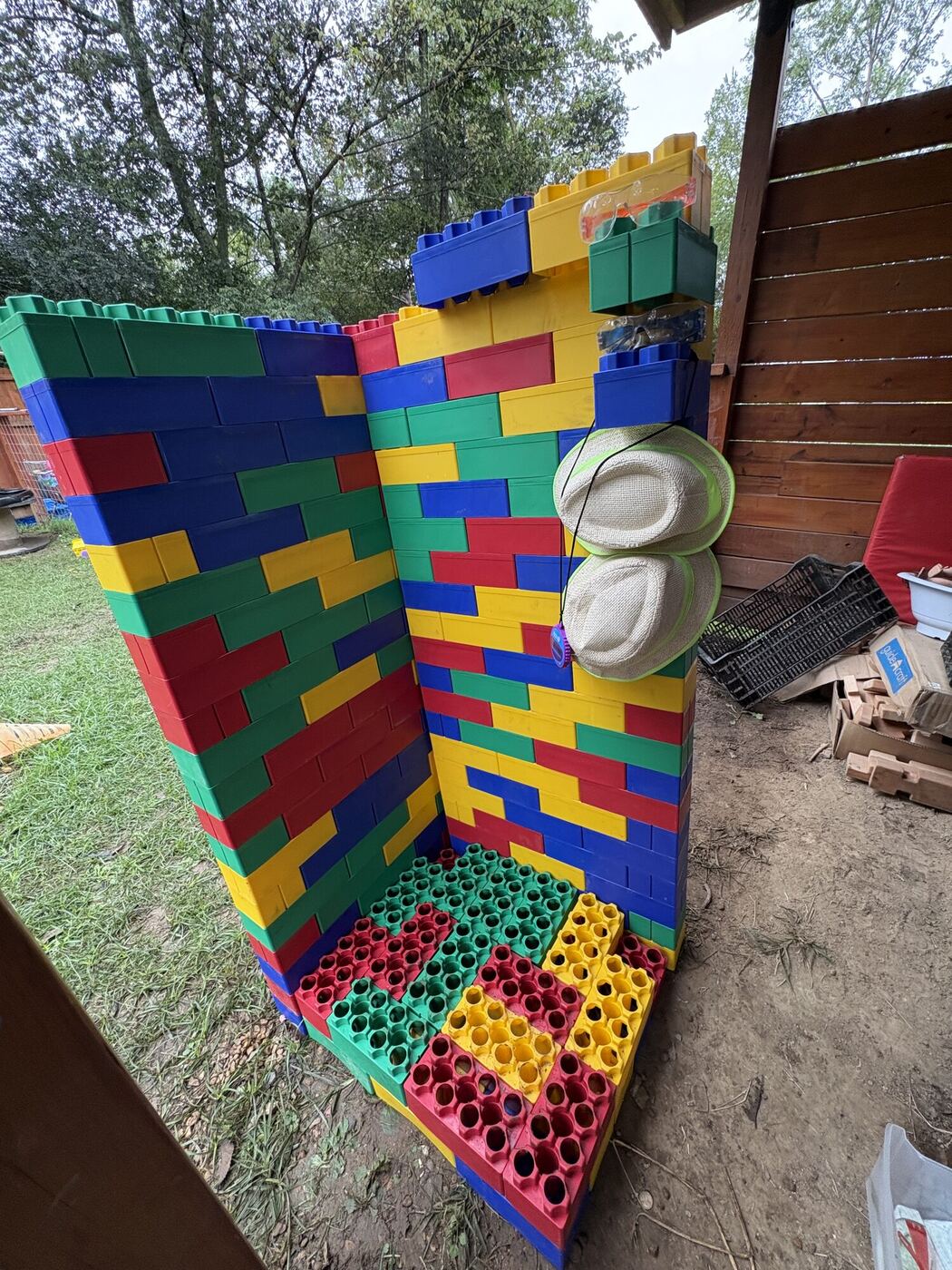 A corner room built from large toy blocks in the play yard, with shelving and hats hung on the wall