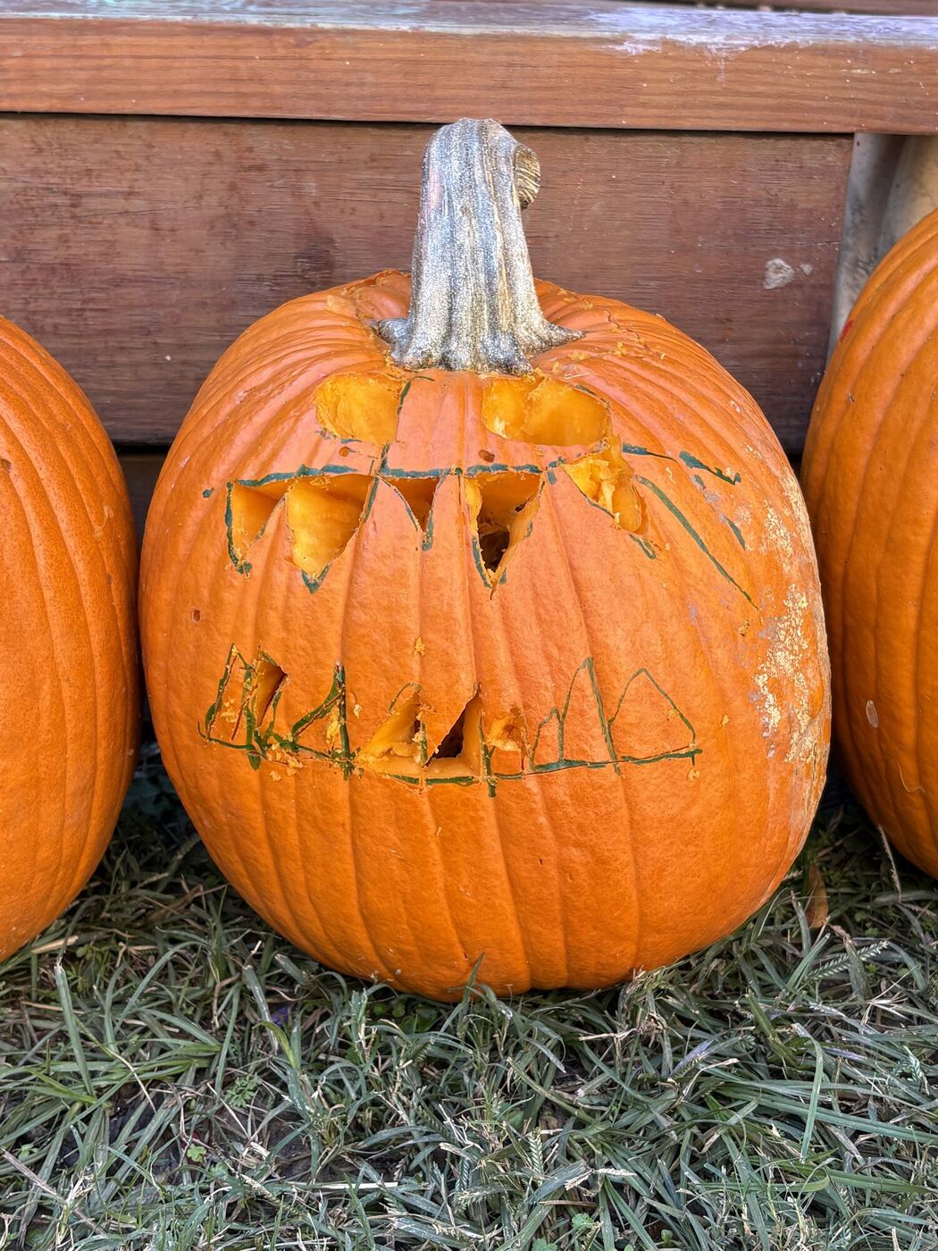 A carved pumpkin with a geometric face, sitting on the grass