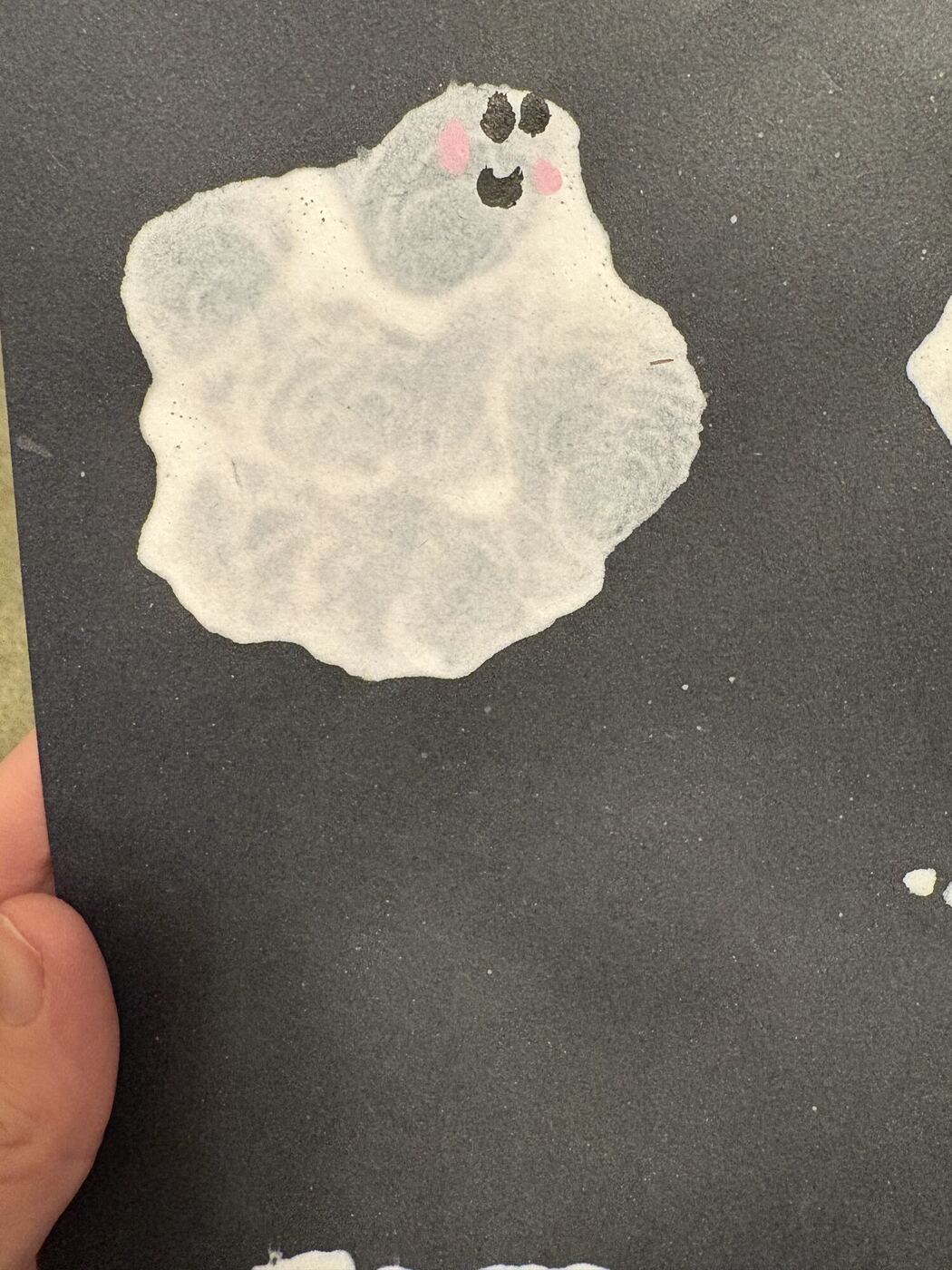 A white ghost blown in paint on black paper, with a small painted face