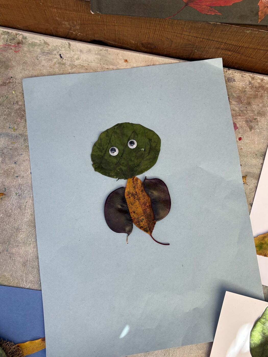 A leaf creature on gray paper with googly eyes