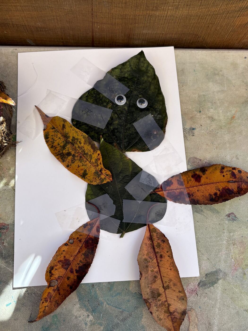 A leaf creature with googly eyes, taped to white paper