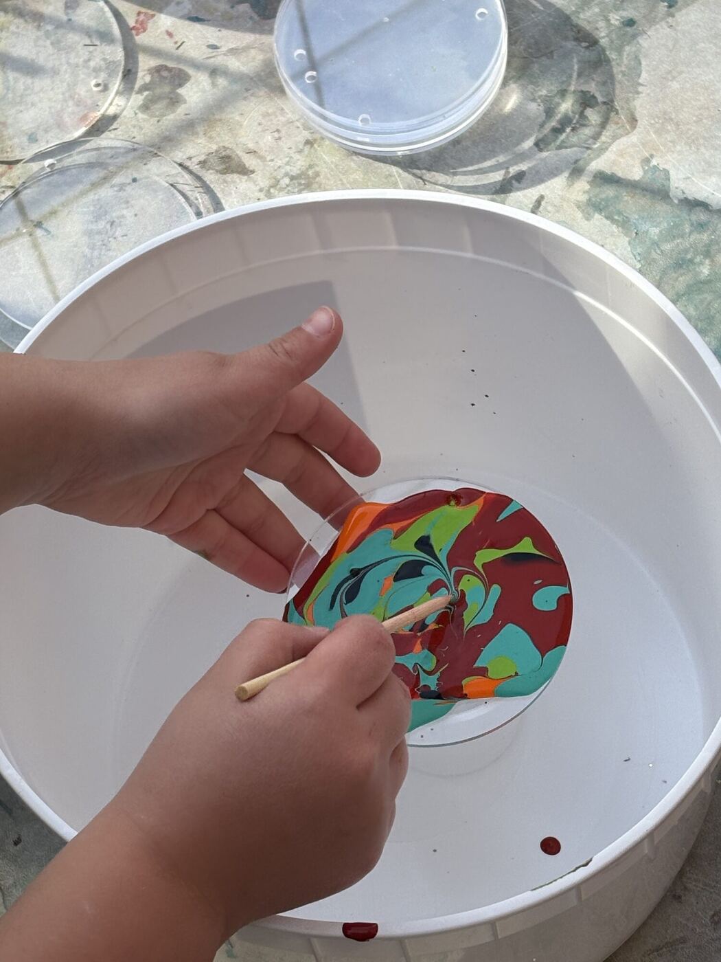 Hands swirling poured paint across a clear disc