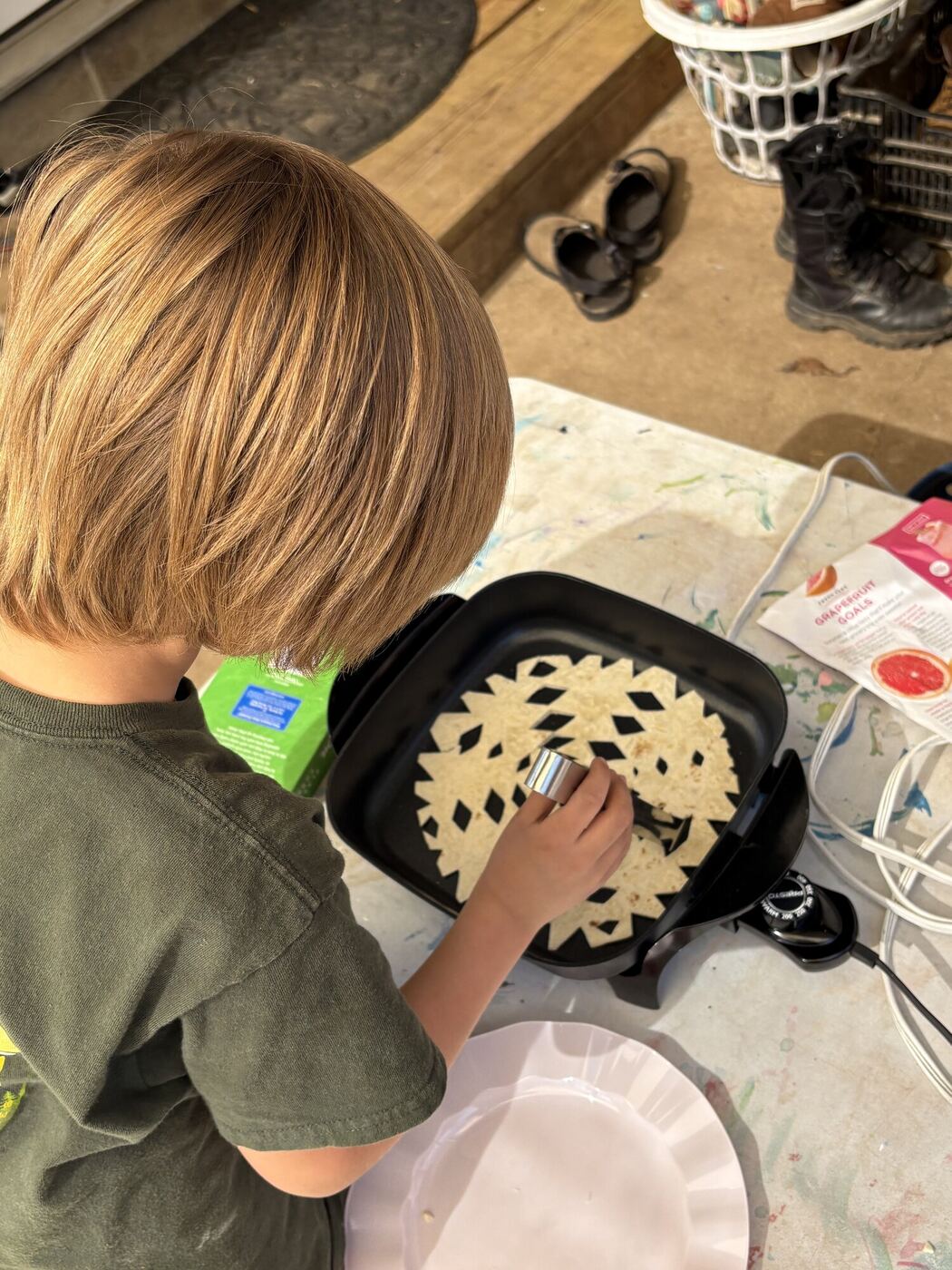 A child seen from behind, cooking a cut-out snowflake tortilla on the skillet