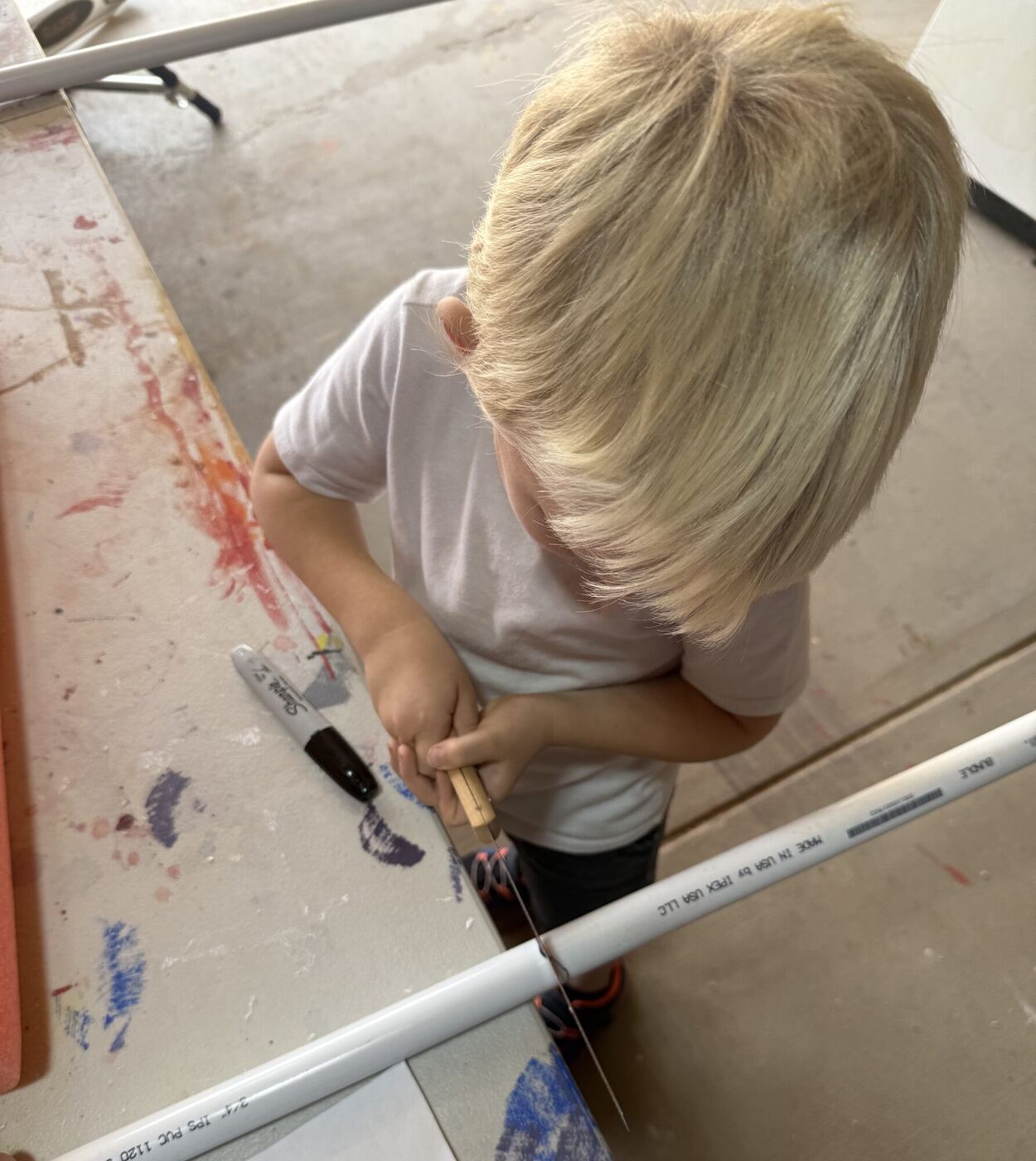 A child seen from above, sawing through the pipe at the edge of a table