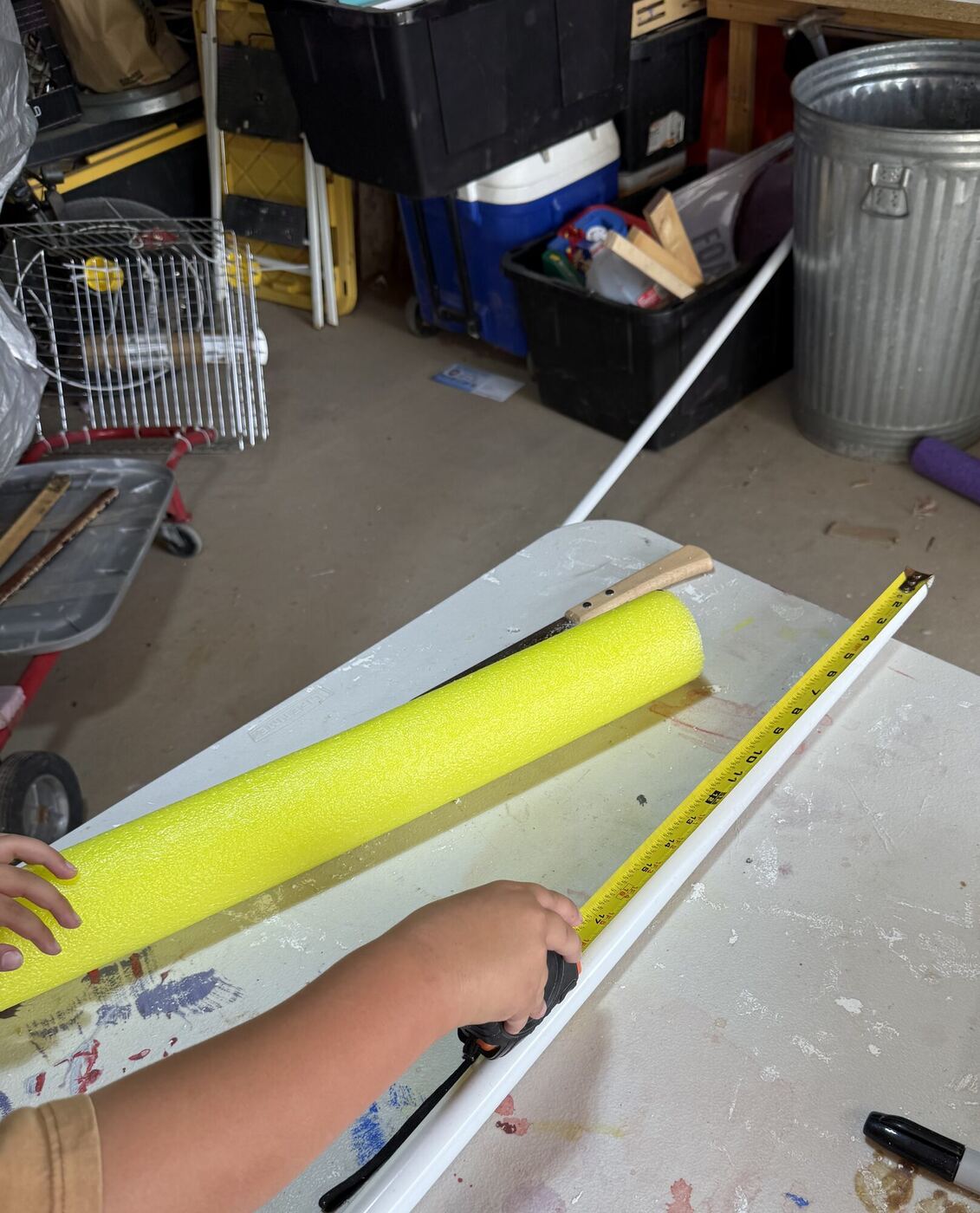 Hands holding a tape measure along a length of white pipe, a foam noodle beside it
