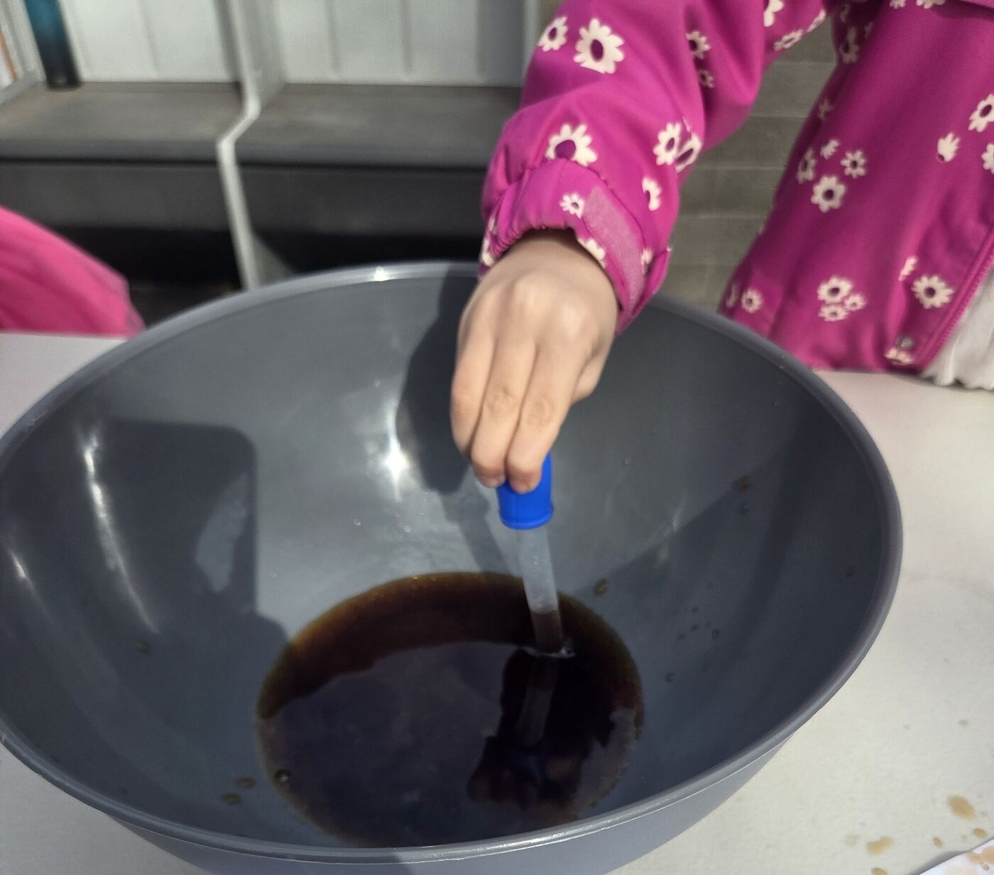 A hand holding a dropper in a bowl of dark soda
