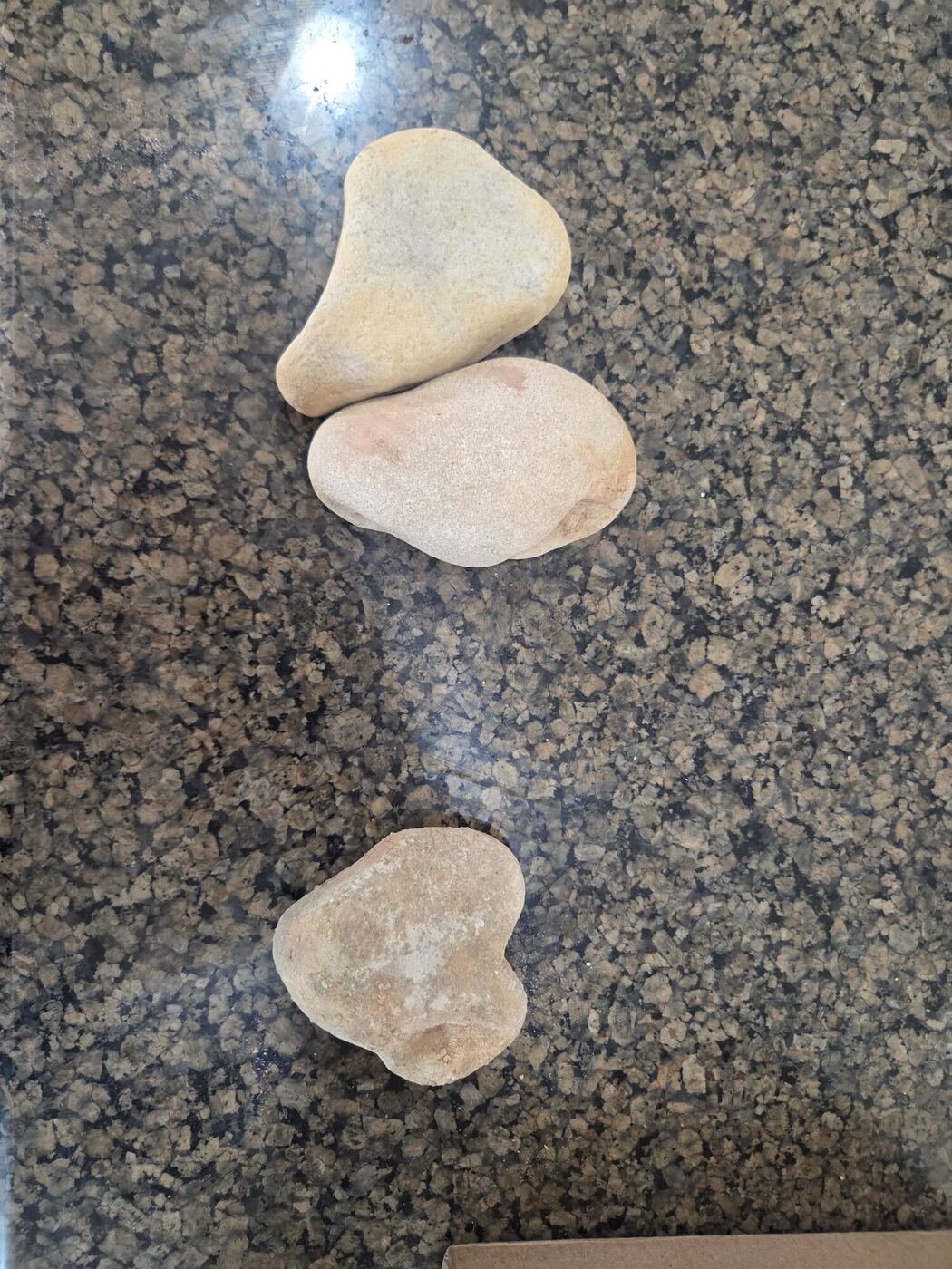 Three pale heart-shaped river rocks on a granite counter