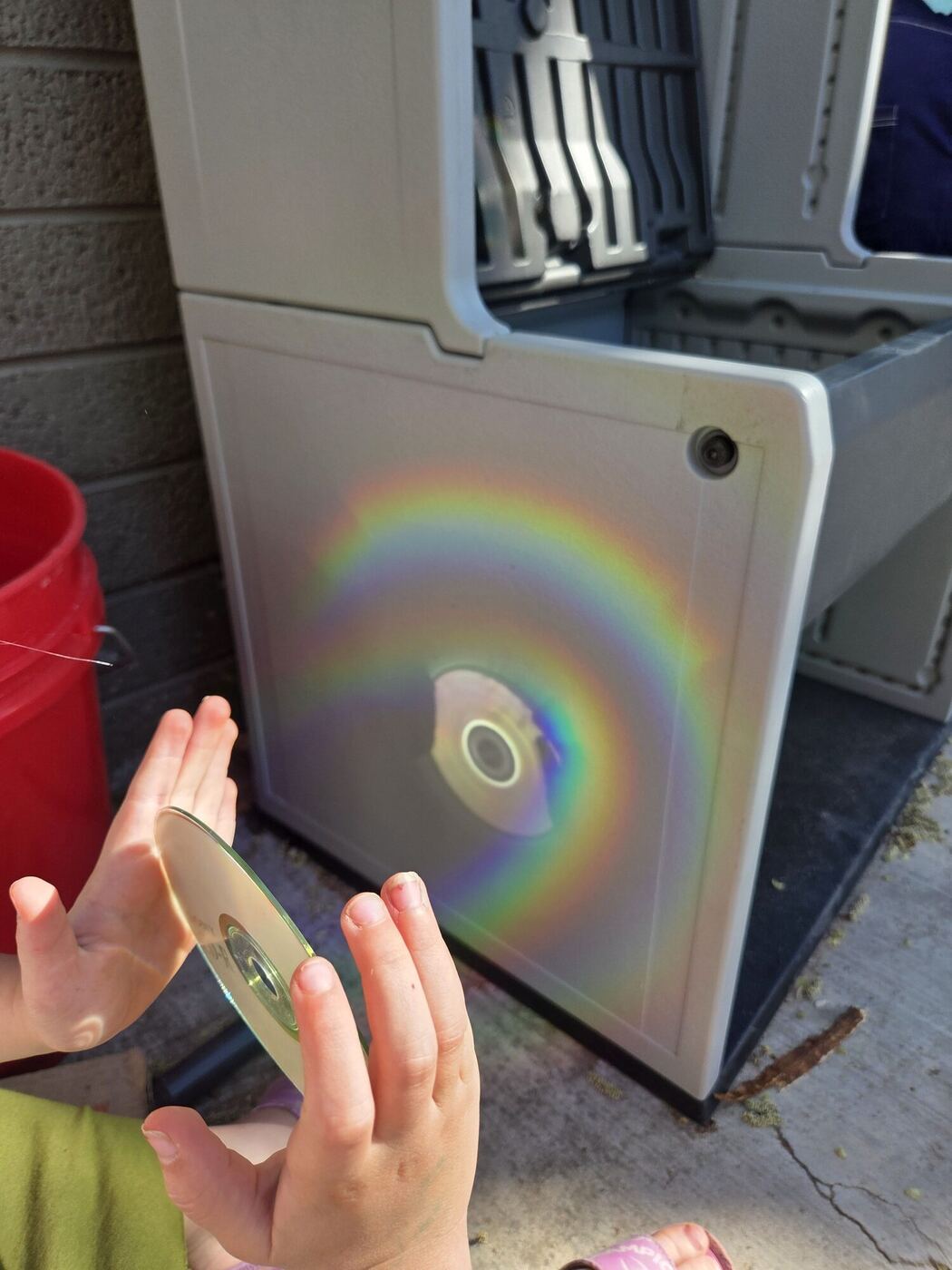 A rainbow cast on a white cabinet by a CD held in the sun