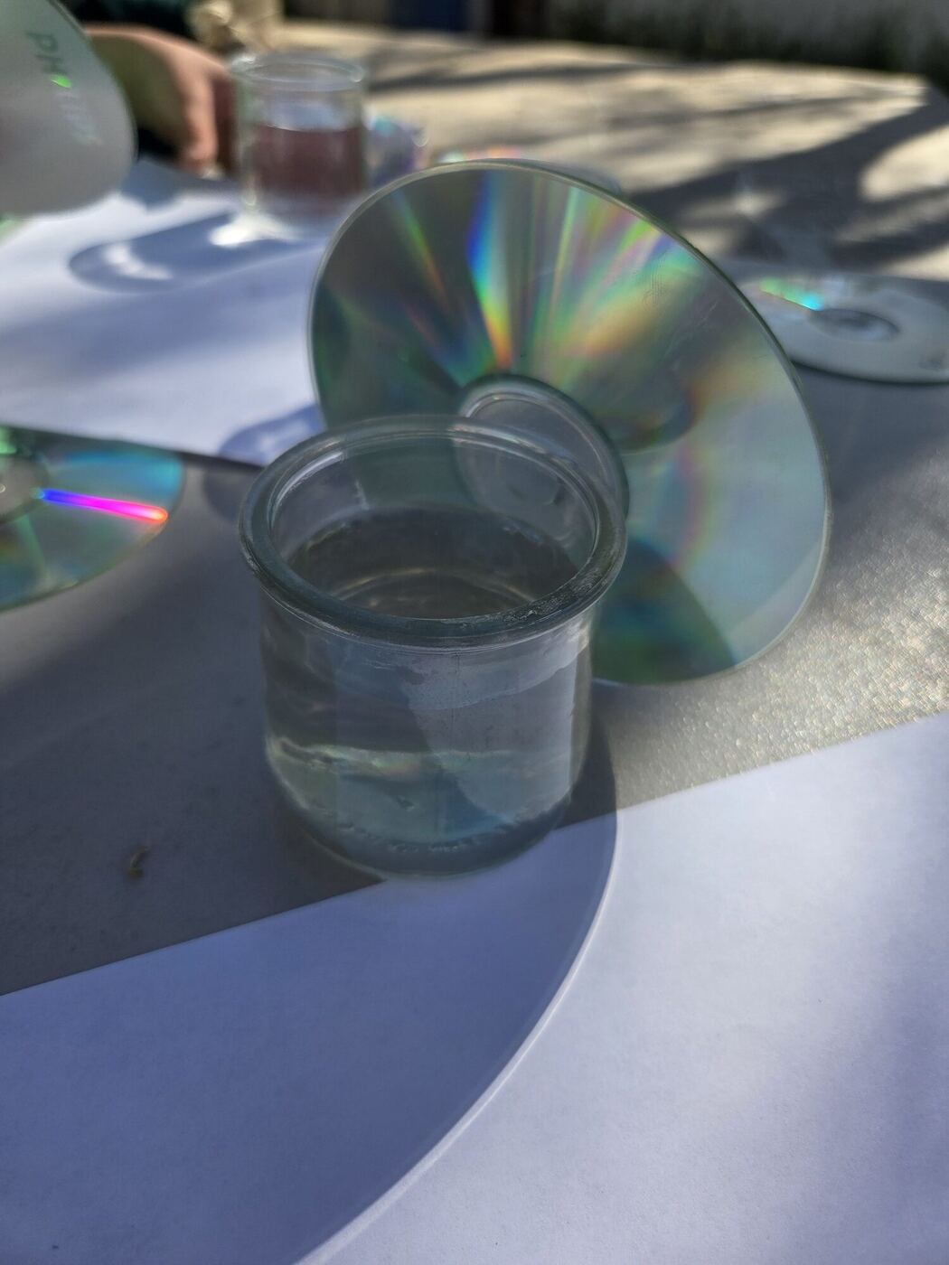 A CD propped against a glass of water on a sunny table