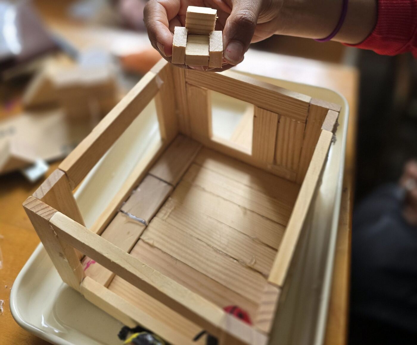 Hands holding a piece of tiny wooden furniture over the model house
