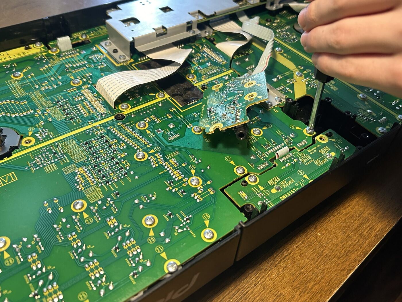 A hand with a screwdriver inside an opened DJ deck, green circuit boards