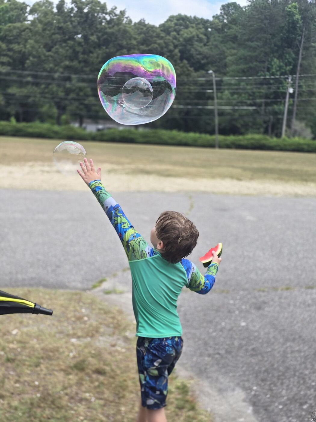 A learner from behind reaching up toward a giant soap bubble, a slice of watermelon in the other hand