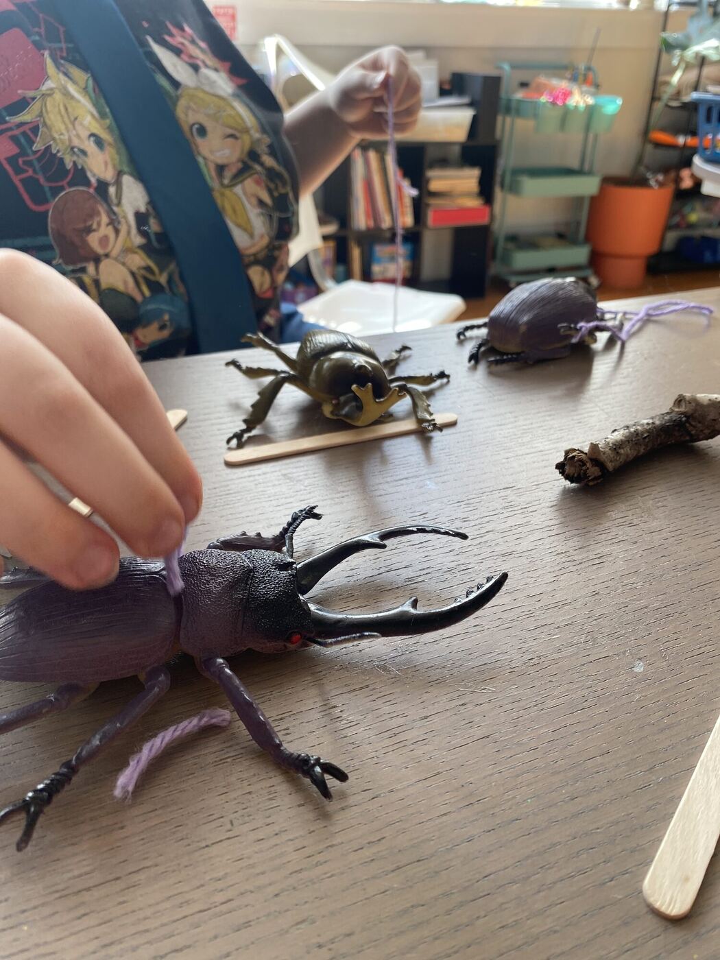 Fingers tying purple yarn to a toy stag beetle on a table