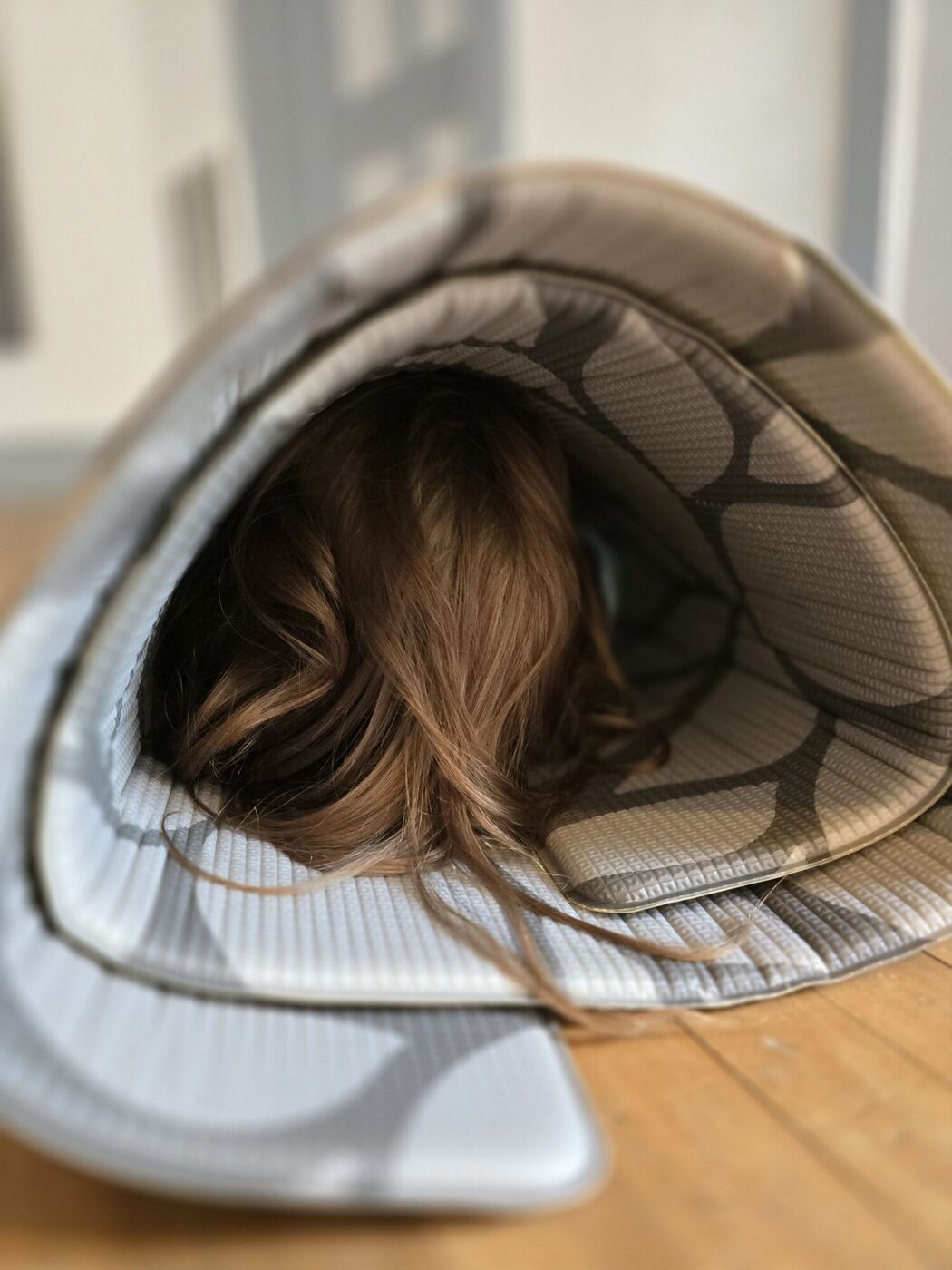 A learner rolled up inside a patterned floor mat, only hair showing