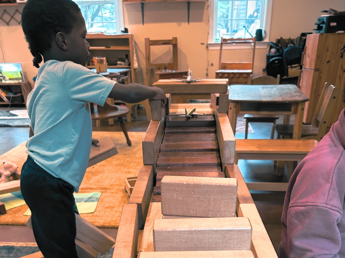 A child adding a block to a long wooden structure they are building
